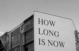 image of how long is now painted on a very large mural wall, on the side of a building. Black text on white background